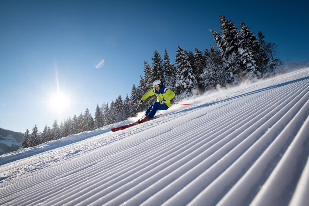 Skifahrer auf perfekt präparierter Piste unter blauem Himmel und Sonnenschein.