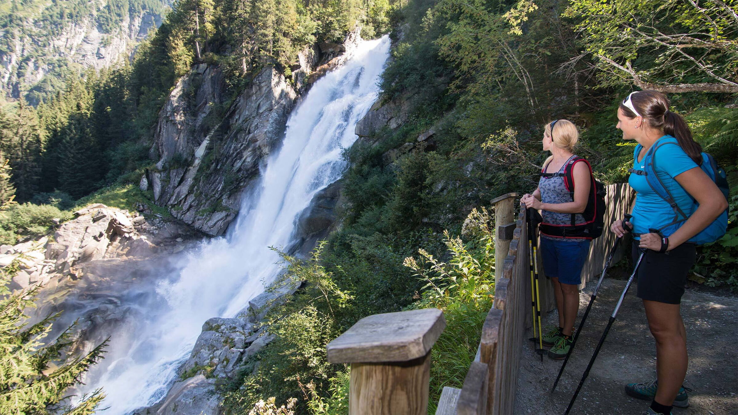 Two hikers contemplate the impressive, rushing Krimml waterfalls in the countryside.