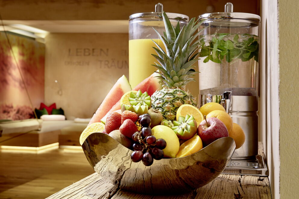 Schale mit frischem Obst, Saft- und Wasserbehälter im stilvollen Wellnessbereich.