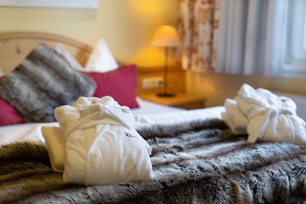 Flauschige Bademäntel auf gemütlichem Bett mit warmem Licht und Fellakzenten.