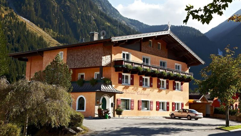 Traditionelles Hotel in malerischer Berglandschaft mit grünen Bäumen und strahlendem Himmel.