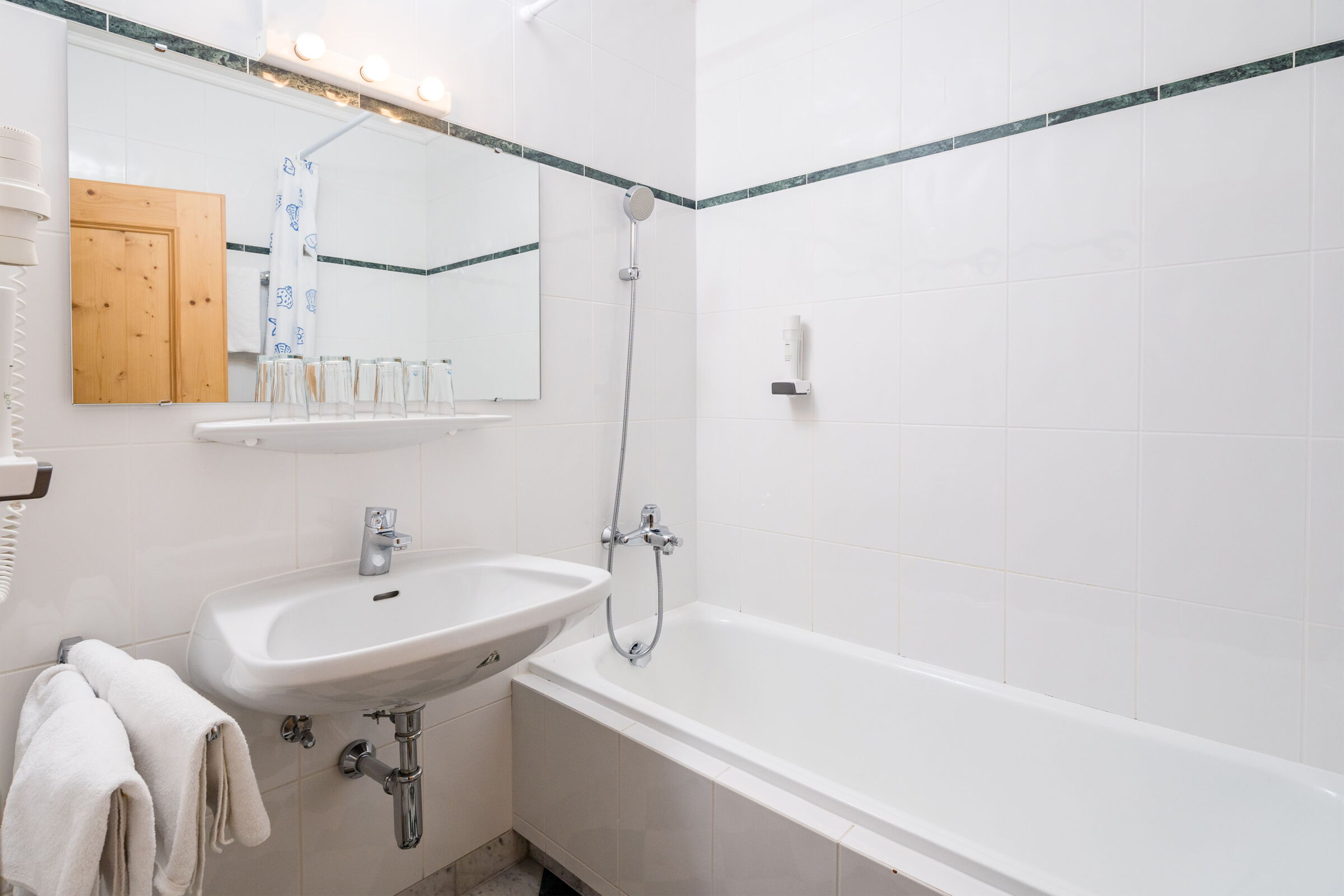 Weiß gefliestes Bad mit Waschbecken, Badewanne und Spiegel, stilvoll und funktional.