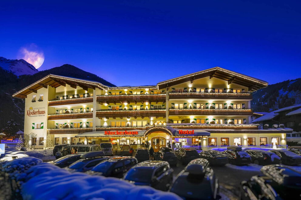 Hotel Klockerhaus leuchtet abends mit verschneiten Bergen im Hintergrund.
