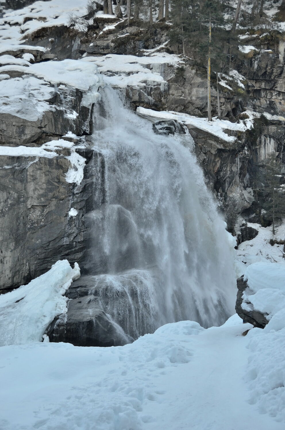 Gefrorener Krimmler Wasserfall umgeben von verschneiten Felsen und winterlicher Landschaft.
