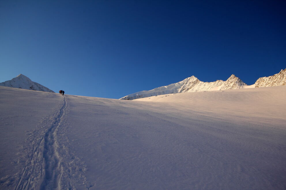Schneebedeckte Berge unter klarem, blauem Himmel mit Fußspuren im Vordergrund.
